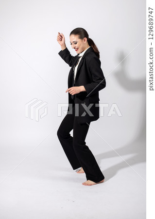 Woman wearing classic black suit and dancing on studio white background Woman wearing classic black suit and dancing on studio white background 129689747