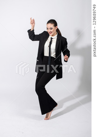 Woman wearing classic black suit and dancing on studio white background 129689749