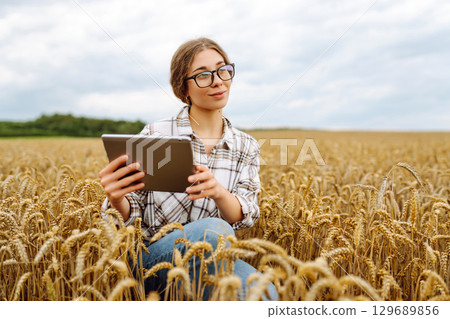 Woman agronomist in a field with a tablet checks the growth of the crop. New harvest concept. 129689856