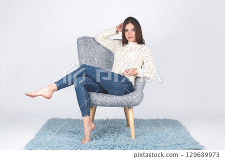 Woman with sweater and jeans sitting on armchair Woman with sweater and jeans sitting on armchair 129689973