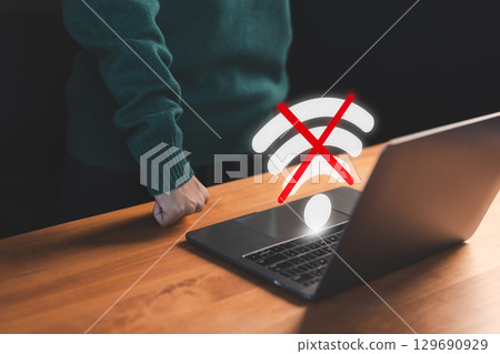 User using a laptop to connect to wifi with a crossed-out Wi-Fi symbol, representing internet disconnection and network failure stress. Concept of frustrated user waiting for connect to wifi. User using a laptop to connect to wifi with a crossed-out Wi-Fi symbol, representing internet disconnection and network failure stress. Concept of frustrated user waiting for connect to wifi. 129690929