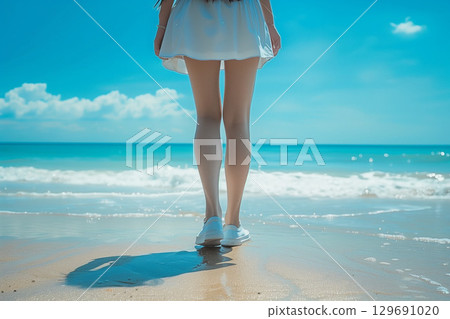 一位女士站在白色沙灘上，背對著藍色的大海 129691020
