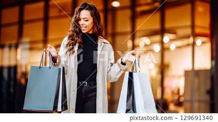 Young woman with shopping bags near mall. Spring Style. Consumerism, purchases, shopping, lifestyle Young woman with shopping bags near mall. Spring Style. Consumerism, purchases, shopping, lifestyle 129691340