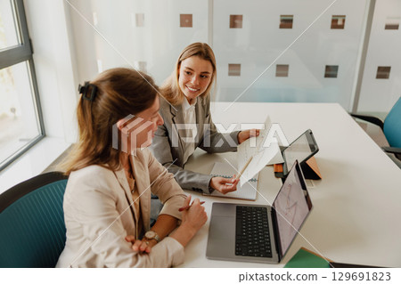 A Business Meeting is Happening Between Two Professional Women in a Modern Office Setting 129691823