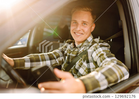 Man using smartphone while sitting in car parked in urban area during daytime. Lifestyle concept. Man using smartphone while sitting in car parked in urban area during daytime. Lifestyle concept. 129692176