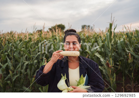 Agronomist inspecting a corn field and eating an ear of corn 129692985