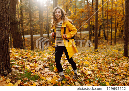 Hiking in autumn forest. Smiling tourist in bright coat walks through autumn park in sunny weather. 129693322