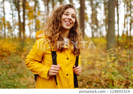 Hiking in autumn forest. Smiling tourist in bright coat walks through autumn park in sunny weather. Hiking in autumn forest. Smiling tourist in bright coat walks through autumn park in sunny weather. 129693324