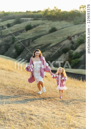 A young mother and daughter are walking in nature among the mountains in beautiful identical sweaters 129693376