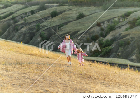 A young mother and daughter are walking in nature among the mountains in beautiful identical sweaters 129693377