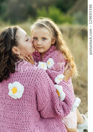 A young mother and daughter are hugging in nature among the mountains in beautiful identical sweaters A young mother and daughter are hugging in nature among the mountains in beautiful identical sweaters 129693396