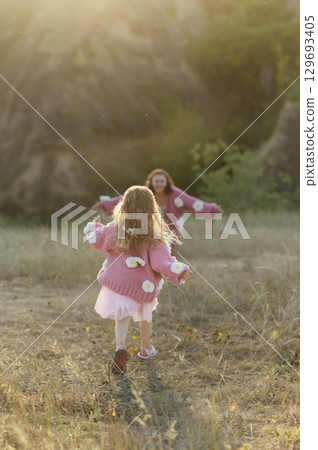A young mother and daughter are walking in nature among the mountains in beautiful identical sweaters A young mother and daughter are walking in nature among the mountains in beautiful identical sweaters 129693405