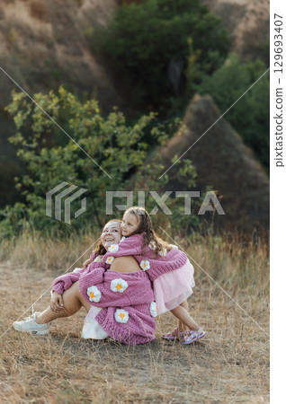 A young mother and daughter are hugging in nature among the mountains in beautiful identical sweaters A young mother and daughter are hugging in nature among the mountains in beautiful identical sweaters 129693407