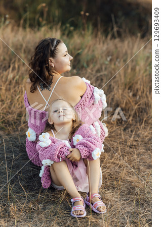 A young mother and daughter are walking in nature among the mountains in beautiful identical sweaters 129693409