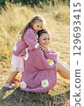 A young mother and daughter are hugging in nature among the mountains in beautiful identical sweaters 129693415