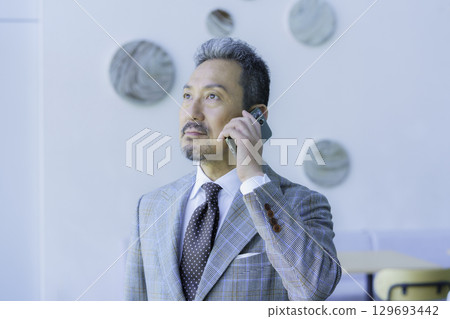 A middle-aged man wearing a suit talking on his smartphone. Photo courtesy of Sky Perfect TV Tokyo Media Center 129693442