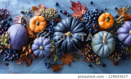 Vibrant pumpkins of various colors and sizes are artistically arranged alongside clusters of berries on a blue wooden surface. Autumn background. 129693637