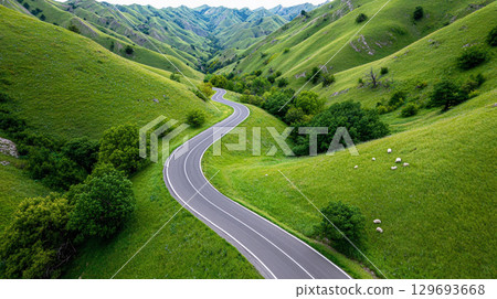 Winding road through lush green hills under a clear blue sky during a sunny day in a remote countryside landscape 129693668
