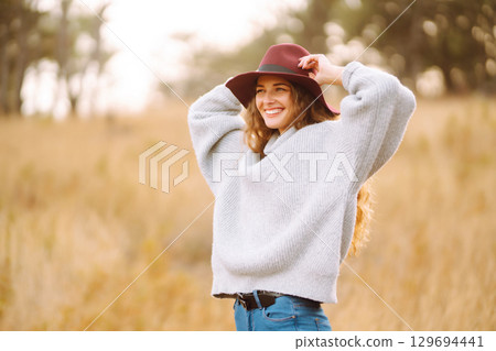 Stylish woman in sweater and hat enjoys autumn nature. People, freedom, lifestyle, travel concept. Stylish woman in sweater and hat enjoys autumn nature. People, freedom, lifestyle, travel concept. 129694441