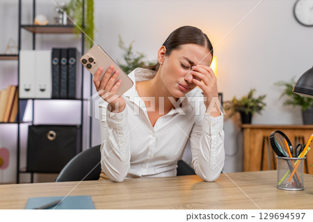 Young businesswoman frowns at smartphone sees game loss failed order budget blown client rejection Young businesswoman frowns at smartphone sees game loss failed order budget blown client rejection 129694597