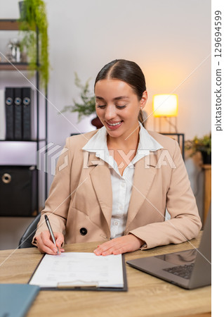 Young businesswoman reads contract terms carefully and signs name at end of page with steady hand Young businesswoman reads contract terms carefully and signs name at end of page with steady hand 129694599