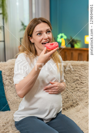 Pregnant woman bites pink donut laughs enjoys sweet treat keeps fun memory forever Pregnant woman bites pink donut laughs enjoys sweet treat keeps fun memory forever 129694661