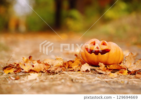 Traditional pumpkin as jack o'lantern, autumn fallen leaves lie on the park. Halloween greeting card Traditional pumpkin as jack o'lantern, autumn fallen leaves lie on the park. Halloween greeting card 129694669