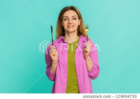 Woman holding fork and knife expressing hunger showing time to eat gesture with eager facial emotion Woman holding fork and knife expressing hunger showing time to eat gesture with eager facial emotion 129694730
