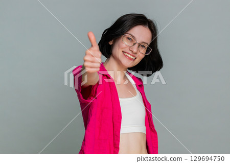 Young woman smiling showing thumbs up like gesture expressing approval agreement satisfaction sign 129694750