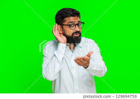 Indian man frowning and holding hand to ear pretending not to hear showing confusion, surprise Indian man frowning and holding hand to ear pretending not to hear showing confusion, surprise 129694759