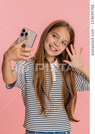 Child girl kid happily receiving video call on smartphone joyfully waving and talking with friend Child girl kid happily receiving video call on smartphone joyfully waving and talking with friend 129694766