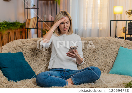 Adult woman disappointed by bad news on smartphone at home sighs with frustration emotional reaction Adult woman disappointed by bad news on smartphone at home sighs with frustration emotional reaction 129694788