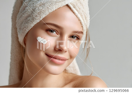A soft towel frames a smiling face, as cream is applied for a simple skin care routine. 129695066
