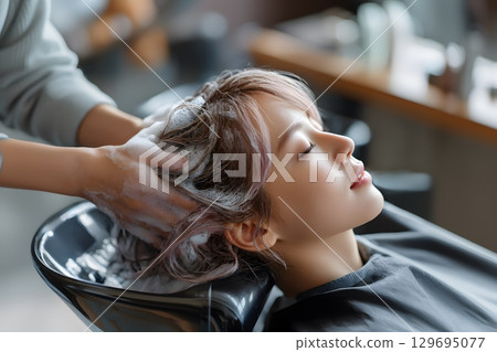 A person receives a relaxing hair wash treatment at a salon, with hands gently shampooing the head in a modern basin. 129695077