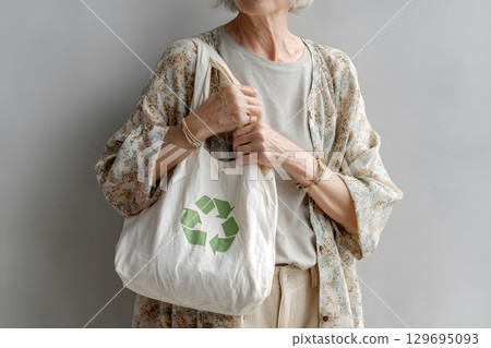 A person holds a plain reusable fabric bag showing a bright green recycle symbol, promoting eco friendly choices and a sustainable environment. 129695093