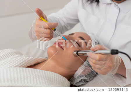 Injection-free mesotherapy or electroporation, beautician makes woman face therapy in clinic salon 129695143