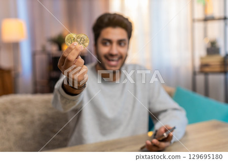 Young Indian man celebrating cryptocurrency win, showing bitcoin after checking exchange charts Young Indian man celebrating cryptocurrency win, showing bitcoin after checking exchange charts 129695180