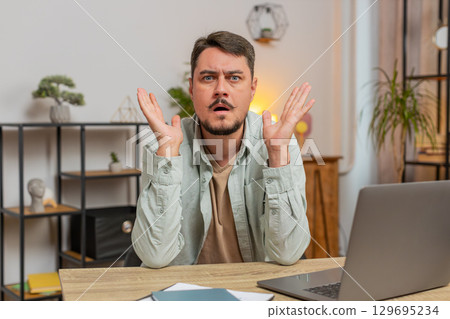 Shocked young man becoming surprised by lottery results, bad fortune, loss, unlucky news at home Shocked young man becoming surprised by lottery results, bad fortune, loss, unlucky news at home 129695234