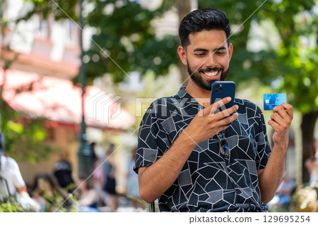 Indian man using credit bank card smartphone transferring money purchases online shopping outdoors 129695254
