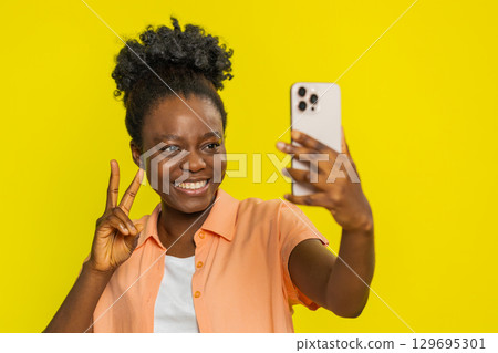 African American woman smiling with smartphone, taking selfie, joyful expression, confident pose 129695301
