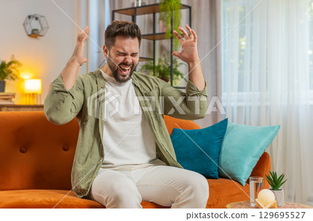 Sad young man feeling loneliness, nervous breakdown, crying shouting on sofa in living room at home 129695527