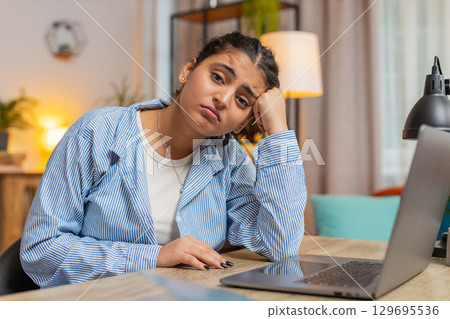 Sad Indian young woman freelancer looks pensive thinks over life concerns sitting at desk at home Sad Indian young woman freelancer looks pensive thinks over life concerns sitting at desk at home 129695536