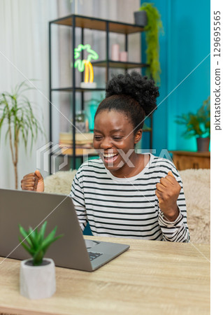 African American woman celebrating good news online email laptop screen happy victory win indoors 129695565