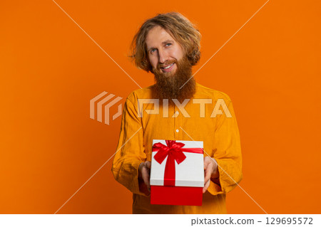 Smiling young man presenting birthday gift present box stretches out hands, promotion discount sale 129695572