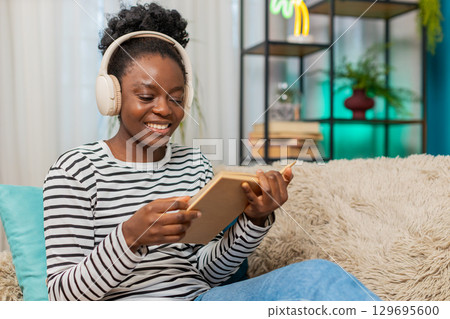African American woman young adult reading novel, deeply focused, sitting on sofa, relaxing at home African American woman young adult reading novel, deeply focused, sitting on sofa, relaxing at home 129695600