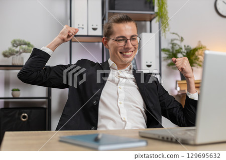 Stylish young Caucasian manager in suit working on laptop netbook shocked by sudden victory at home 129695632