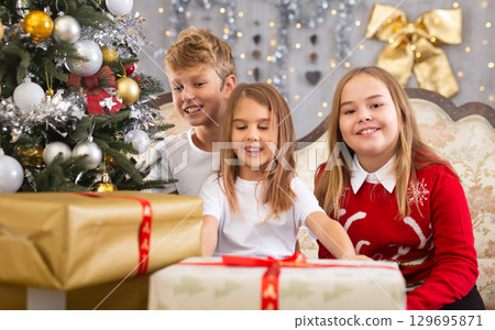 Two girls and boy holding gift in Christmas interior 129695871
