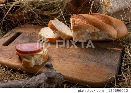 Sandwich with butter and cheese on a wooden cutting board. Baguette and board placed on hay, rustic countryside food composition. 129696030
