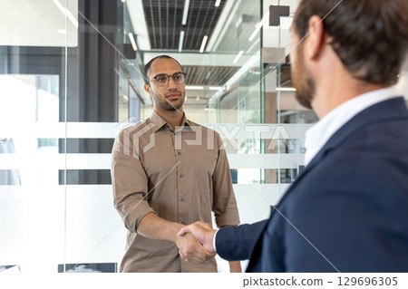 Two professionals greet each other with a handshake in a contemporary office setting, fostering collaboration. Two professionals greet each other with a handshake in a contemporary office setting, fostering collaboration. 129696305