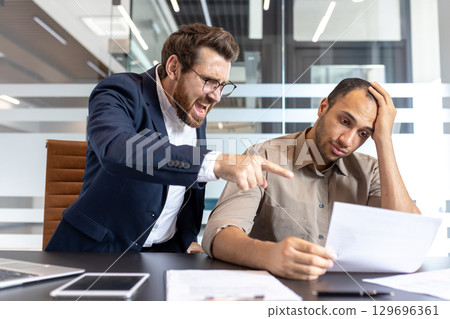 A frustrated boss yells at an employee while pointing at a document in an office 129696361